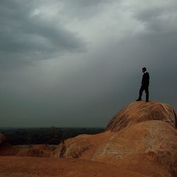 Low angle view of man standing on rock by sea against cloudy sky at dusk