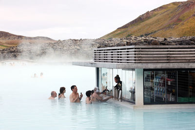 People relaxing in swimming pool against mountain