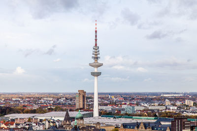 Communications tower in city against cloudy sky