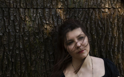 Portrait of young woman against tree trunk