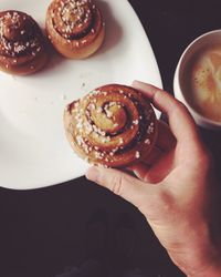Low section of woman holding cinnamon bun over plate