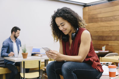 Young woman using smart phone while sitting on laptop