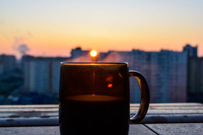Close-up of coffee cup against sky during sunset
