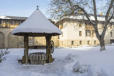 Snow covered house by building against sky