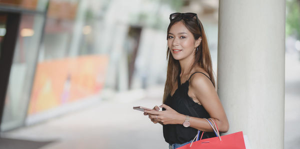 Portrait of young woman using mobile phone by column