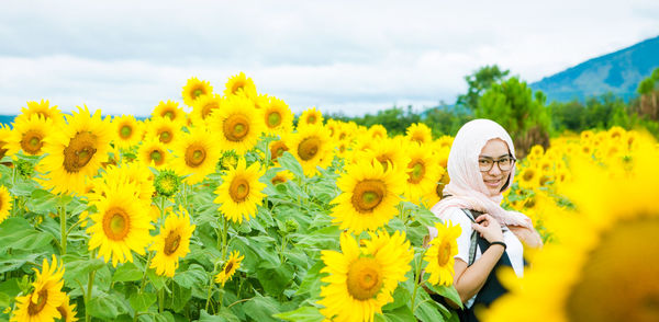 Portrait of woman at sunflower field against sky