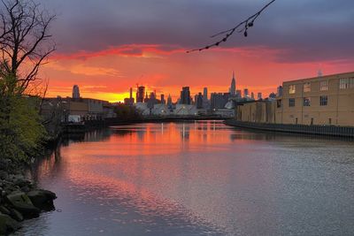 Scenic view of river by buildings against sky during sunset