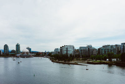 Buildings by river against sky in city