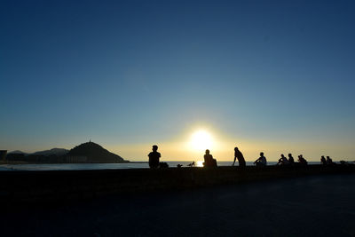 Silhouette people on lake against sky during sunset