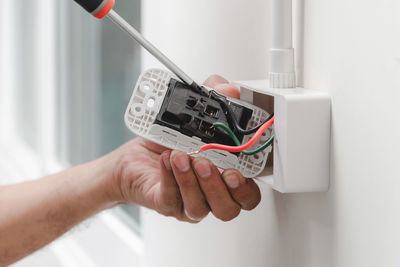 Cropped hands of male electrician repairing electrical outlet on wall