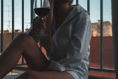 Midsection of woman holding wineglass while sitting against railing