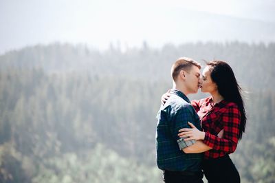 Side view of young couple kissing while standing in forest