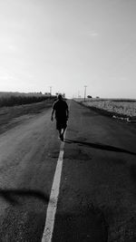 Rear view of man walking on road against sky during sunny day