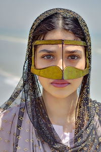 Close-up portrait of young woman wearing traditional clothing standing at beach against sky