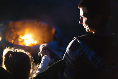 Dad and daughter sit at night by the fire in the open air in the summer in nature. family camping