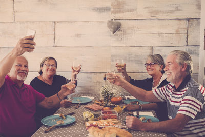 Happy friends toasting drinks while taking selfie at table