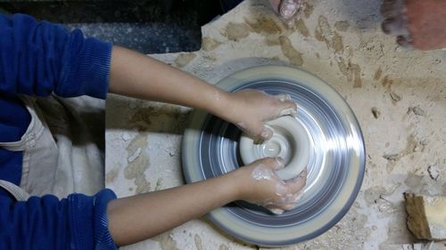 Directly above view of woman molding clay on pottery wheel at workshop