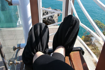 Low section of woman sitting on railing by sea