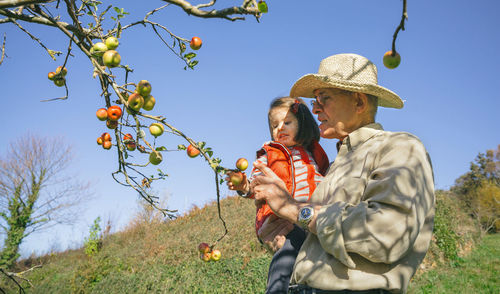 Grandfather with granddaughter picking apple on tree