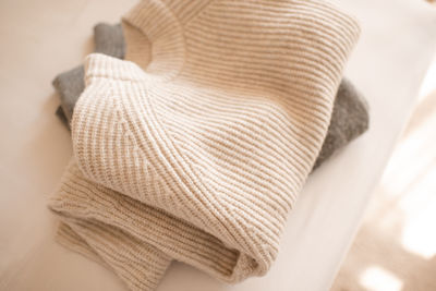 Stack of knitted wool textile sweaters clothes on white blanket in bed at home room close up