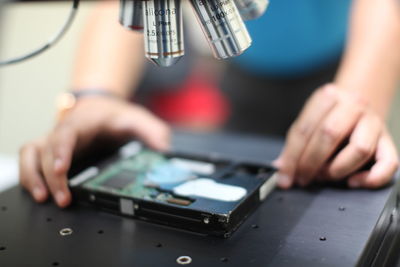 Close-up of hands with hard drive below microscope