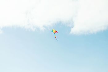 Low angle view of multi colored kite flying against cloudy sky