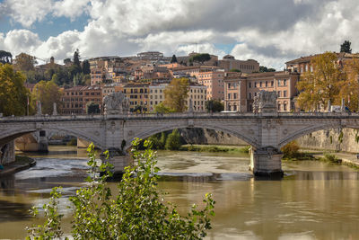 Arch bridge over river by buildings against sky