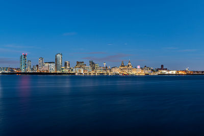 Sea by illuminated buildings against blue sky