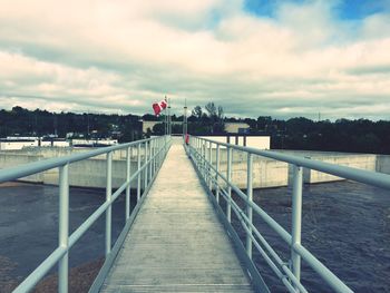 Footbridge over river against cloudy sky