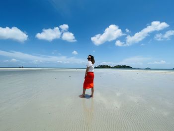 Rear view of woman standing at beach against sky