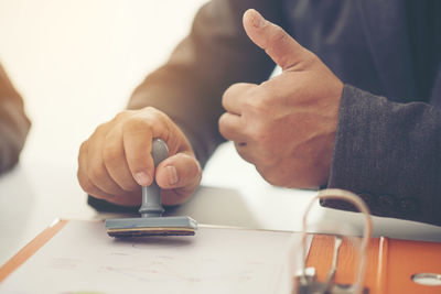 Midsection of lawyers holding rubber stamp while showing thumbs up at desk in office