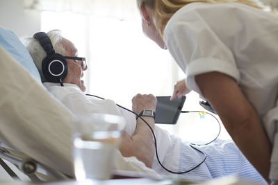 Side view of female nurse assisting senior man in using digital tablet on hospital bed