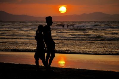 Silhouette couple standing at beach during sunset