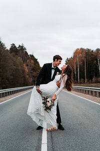 Newlywed couple dancing on road against clear sky