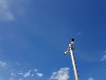 Low angle view of bird perching on statue against blue sky