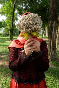 Midsection of woman holding red while standing against plants