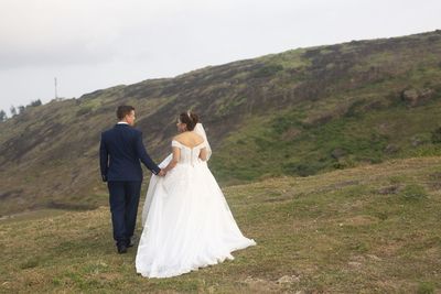 Rear view of bride and groom walking on hillside