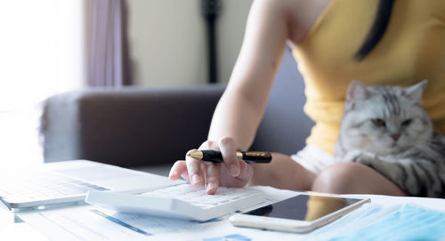 Midsection of woman using smart phone while sitting on table