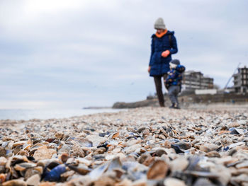 Parent standing with son on pebbles at beach against sky