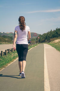 Rear view of woman walking on road against sky