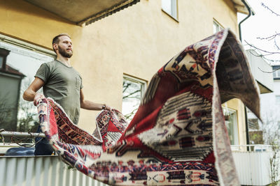 Man dusting carpet while standing on balcony