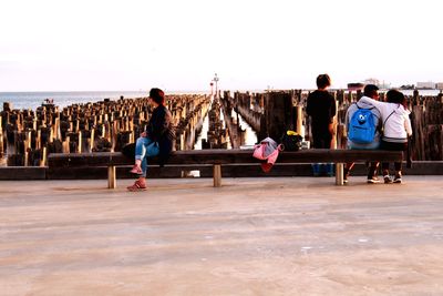 Group of people sitting on beach against clear sky