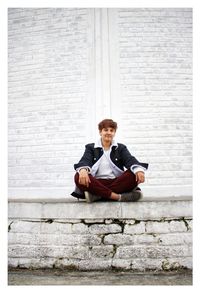 Portrait of young man sitting on wall