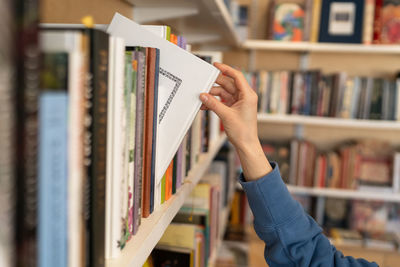 Woman hand picking book from bookshelf in library in university, college, high school or bookshop