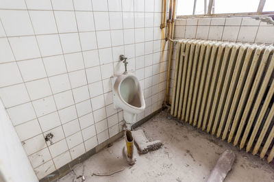 An old abandoned toilet with a completely dusty urinal and a pair of rubber boots on the dirty floor