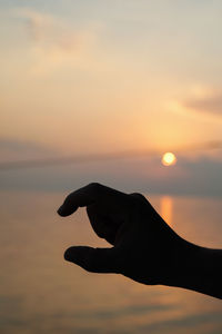 Silhouette hand gesturing at beach against orange sky during sunset