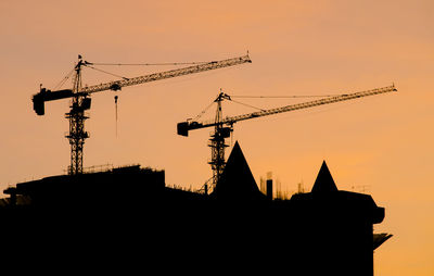 Low angle view of silhouette crane by building against sky during sunset