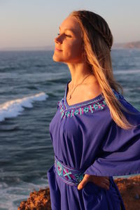 Young woman standing at beach against sky