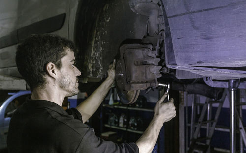 Side view skilled mechanic using ratchet to adjust car brake disc detail while working in garage