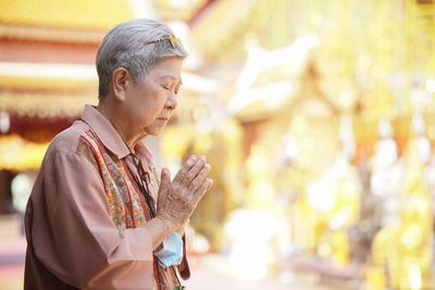 Old asian elder senior woman traveler tourist praying at buddhist temple.